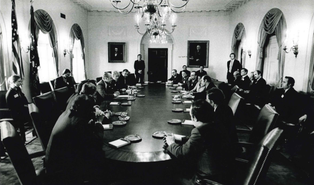 Pres. Ford on the left side of a large table, at the center, with Soviet journalists opposite him.